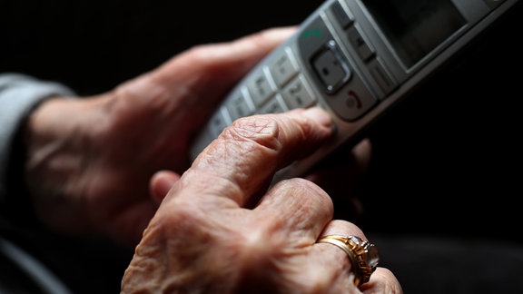 Eine ältere Frau tippt auf einem schnurlosen Festnetztelefon. 