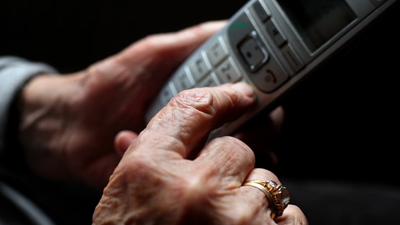 Eine ältere Frau tippt auf einem schnurlosen Festnetztelefon. 