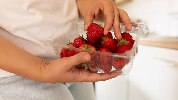 Frau nimmt Erdbeeren aus Plastikbehälter