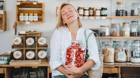 Eine Frau in einem Geschäft hält lächelnd ein Glas mit geschnittenen Erdbeeren.