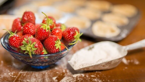 Eine Schüssel Erdbeeren neben Backform und Mehlschaufel