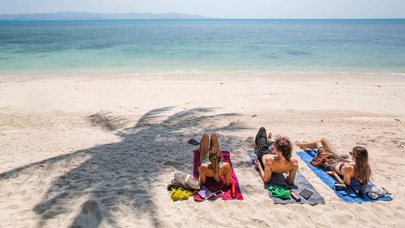 Drei Menschen liegen am Strand
