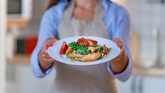Inszeniertes Foto einer Frau, die einen Teller mit Essen in die Kamera hält.