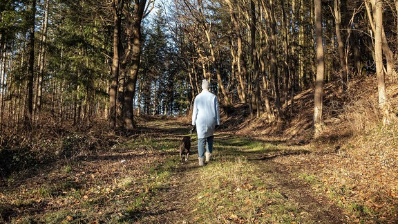 Eine Frau geht mit ihrem Hund auf einem Waldweg