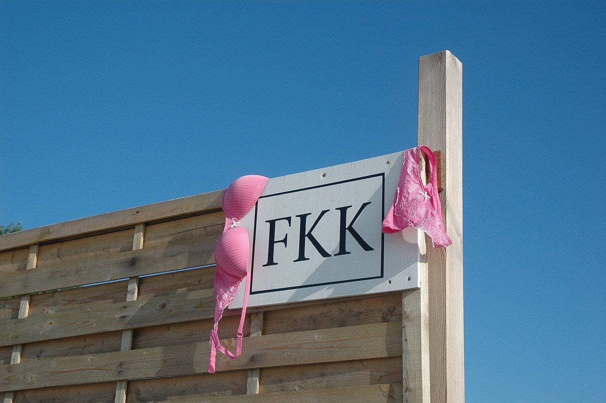 Schild mit der Aufschrift FKK, daneben hängt Unterwäsche