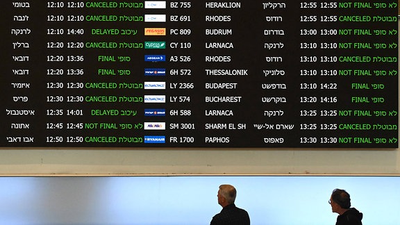 Menschen schauen auf eine Ankunftstafel für gestrichene Flüge auf dem Flughafen Ben Gurion bei Tel Aviv