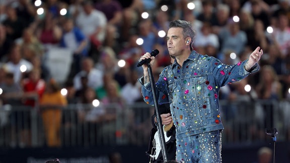 Robbie Williamssingt auf einer Bühne.