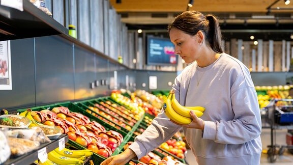 ine Frau begutachtet in einem Supermarkt Bananen.