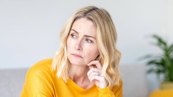Eine blonde Frau sitzt nachdenklich auf einem Sofa