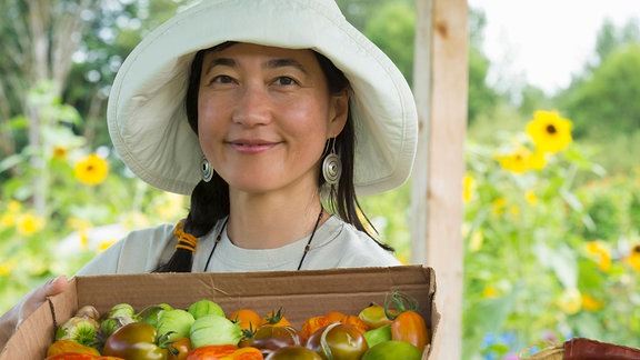 Eine junge Frau mit einem Karton voll Tomaten