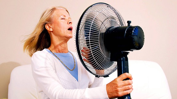 Eine Frau hält sich einen Ventilator vor das Gesicht und genießt den Luftstrom.