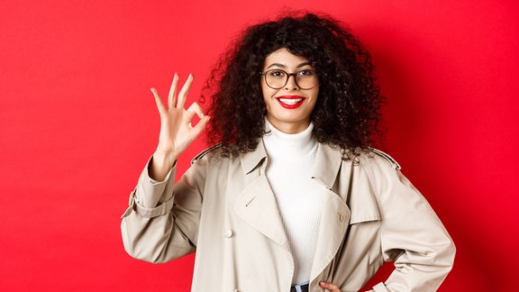 Lächelnde Frau mit Locken und Brille vor roter Wand