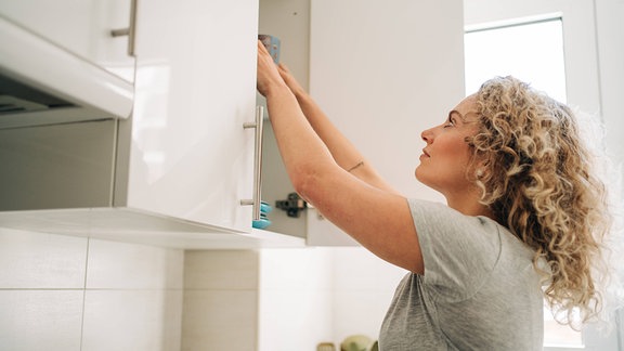 Eine Frau greift in einen Küchenschrank