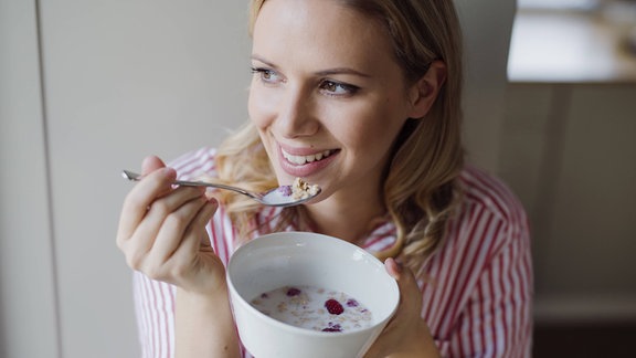 Symbolbild: eine junge Frau isst ein Müsli aus einer Schale.