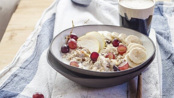 Symbolfoto: Müsli mit Weintrauben, Äpfeln und Bananen und ein Kaffee auf einem Tisch