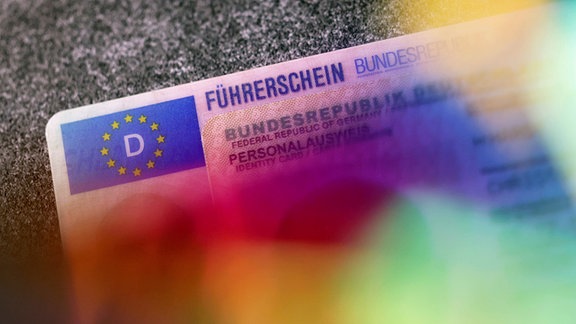 Ein Führerschein liegt unter einem Personalausweis auf einem Tisch. 