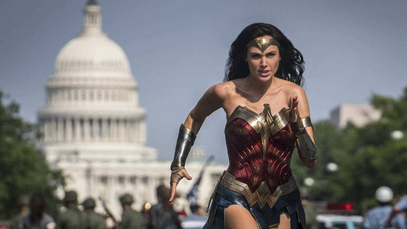 Gal Gadot in ihrer Rolle als Wonder Woman rennt in einem seltsamen Kostüm eine Straße entlang.
