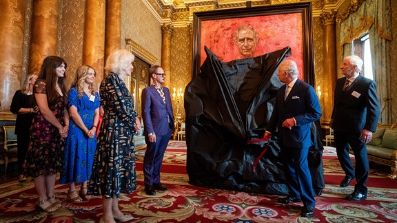 König Charles III. von Großbritannien enthüllt sein Porträtgemälde des Künstlers Jonathan Yeo (3.v.r) in Anwesenheit von Königin Camilla (vorne) im blauen Salon des Buckingham Palace.