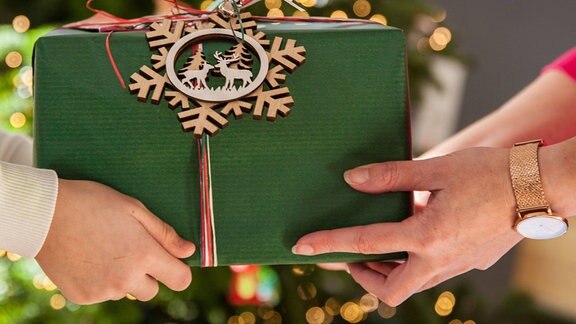 Zwei Personen reichen sich ein weihnachtlich verpacktes Geschenk. 