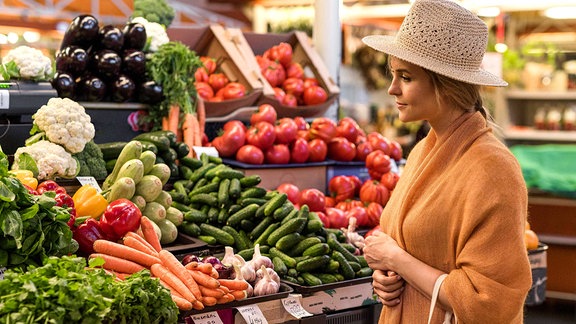 Frau mit Sommerhut in der Gemüseabteilung eines Supermarktes