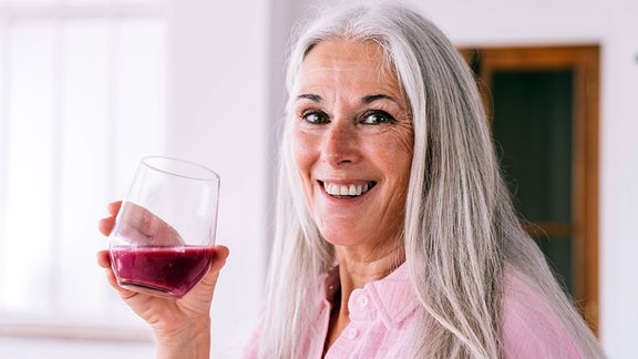 Glückliche Frau, die zu Hause ein Glas mit gesundem Saft hält. (Symbolbild)