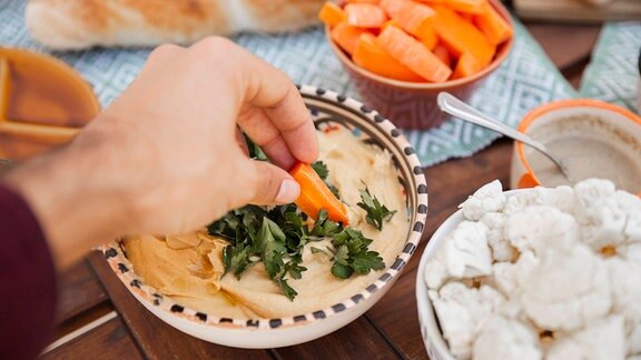 Hand taucht Karotte in Hummus