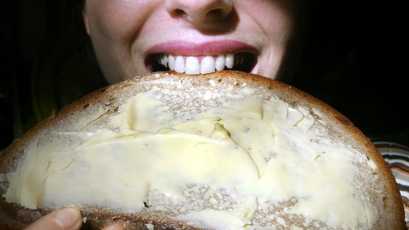 Eine junge Frau beißt in ein dick bestrichenes Butterbrot 