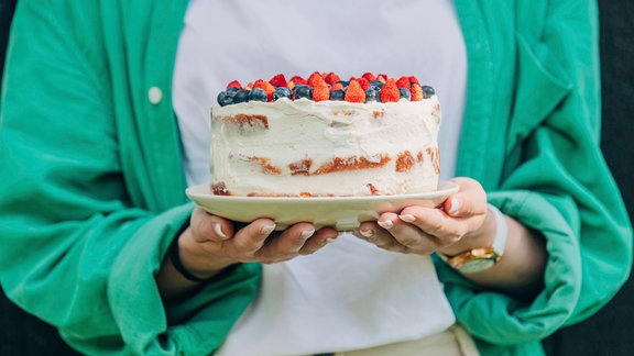 Frau hält einen Kuchen auf beiden Händen
