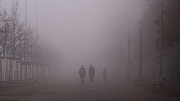 Passanten gehen über einen vernebelten Gehweg