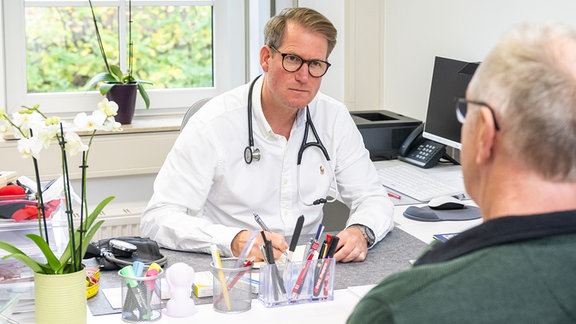 Ein Hausarzt stellt 2022 in einem Sprechzimmer seiner Praxis einem Patienten eine Arbeitsunfaehigkeitsbescheinigung aus.