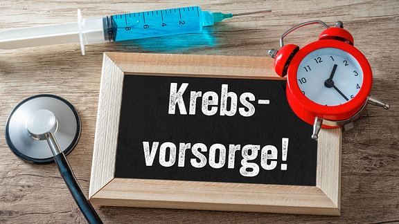 Illustration - Tafel mit Wecker und Spritze mit der Aufschrift: Krebsvorsorge.