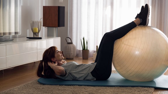 Stock-Foto: eine liegende Frau mit den Beinen auf einem Medizinball