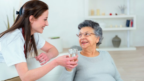 Eine Pflegerin reicht einer älteren Frau ein Glas Wasser