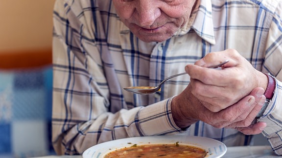 Ein Mann hält sich beim Löffeln einer Suppe die Hand