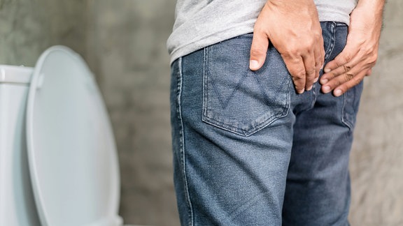Ein Mann steht vor einer Toilette und greift sich ans Gesäß