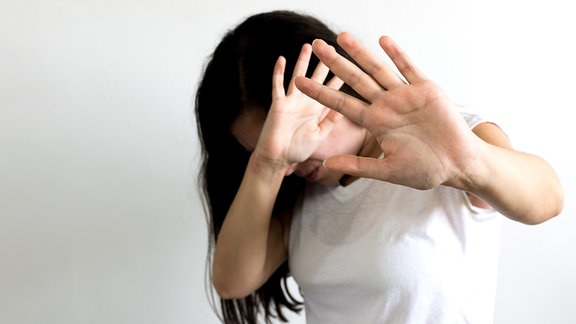 Frau hebt Hände schützend vor Gesicht