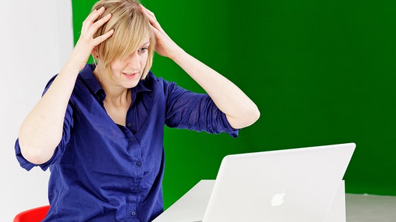 Eine Frau sitzt während einer Online-Auktion gespannt an ihrem Laptop.