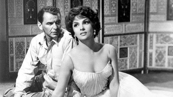 Verführerisch schön sitzt die italienische Schauspielerin Gina Lollobrigida bei Dreharbeiten zu dem Film "Never so Few" (Aufnahme von 1958) neben Filmpartner Frank Sinatra
