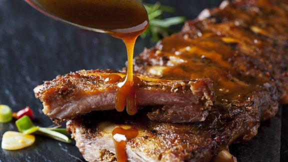 Soße wird auf Grillfleisch getröpfelt.