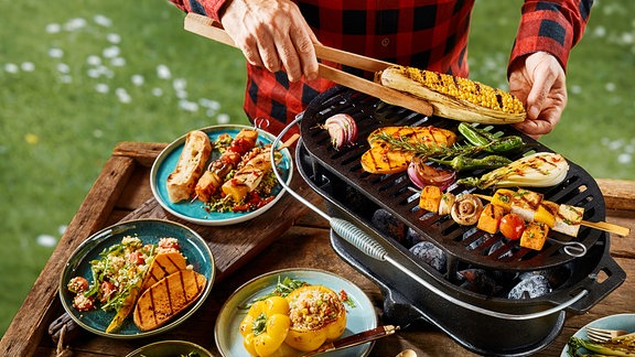 Mann grillt Gemüse über Kohlen im Freien.