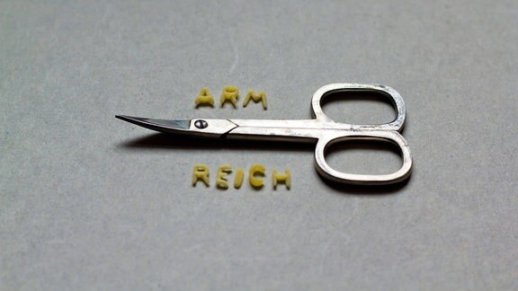 Über einer Schere steht "arm", darunter "reich".