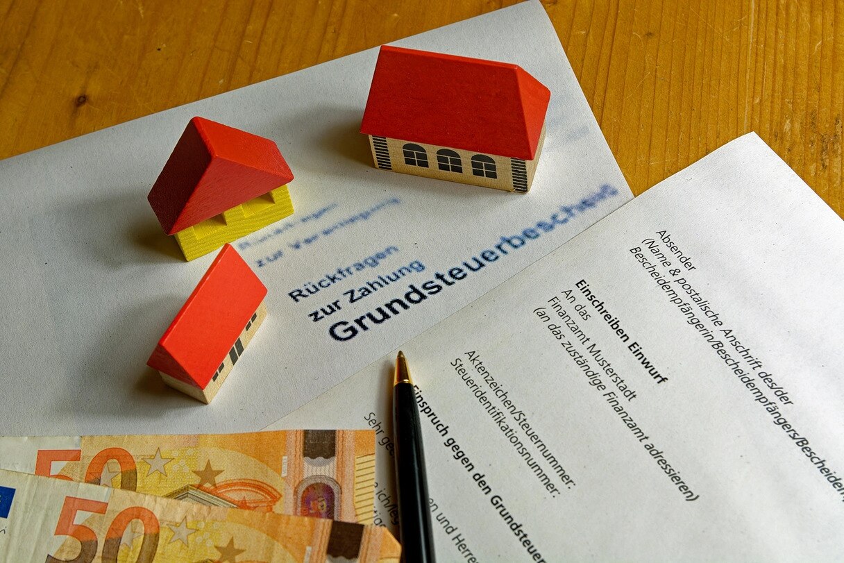 Symbolbild Einspruch gegen Grundsteuerbescheid, Häuser, Stift, Briefe, Geldscheine