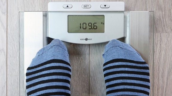 Eine Person wiegt sich. Die Waage zeigt 109,6 Kg.