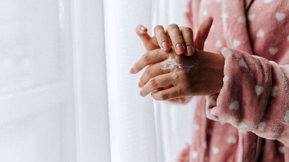 Frau trägt Bademantel und trägt Feuchtigkeitscreme auf die Hand auf.