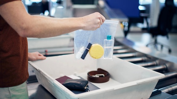 Gegenstände werden am Flughafen in eine Schale auf einem Rollband gepackt.