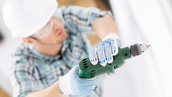 Ein Mann mit Helm bohrt ein Loch in eine Wand mit einer elektrischen Bohrmaschine.