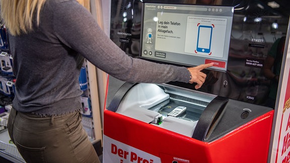 Eine Frau lässt ein altes Handy von einem "EcoATM" in einer MediaMarkt Filiale schätzen. 