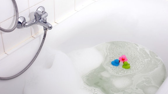 Rosa, grüne und blaue Ente in einer Badewanne, umgeben von Schaum.