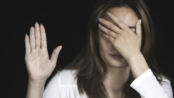 Eine Frau hebt eine Hand, die andere Hand hält sie vor die Augen