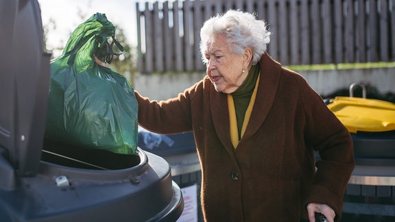 Eine alte Dame entsorgt Müll in einer Mülltonne.